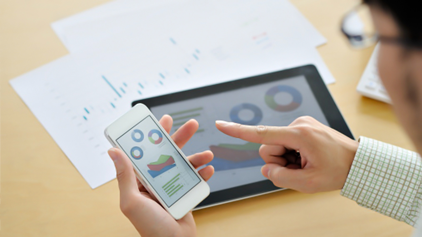 Man working on smartphone showing a business graphic with a tablet on the desk in the background.