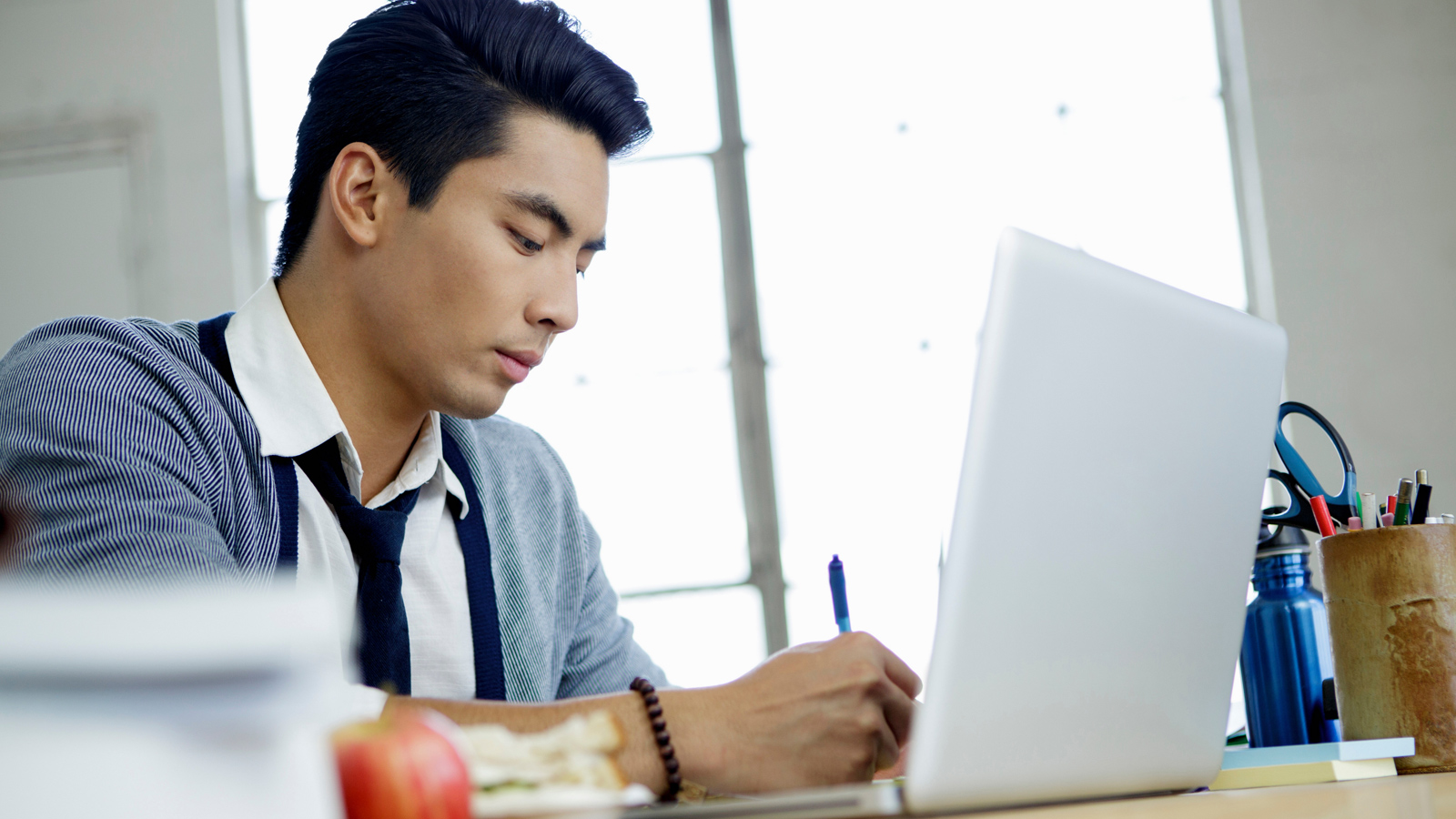 Young man sitting at his desk and working in front of his laptop.