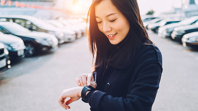 Woman standing in a parking lot looking at her watch.