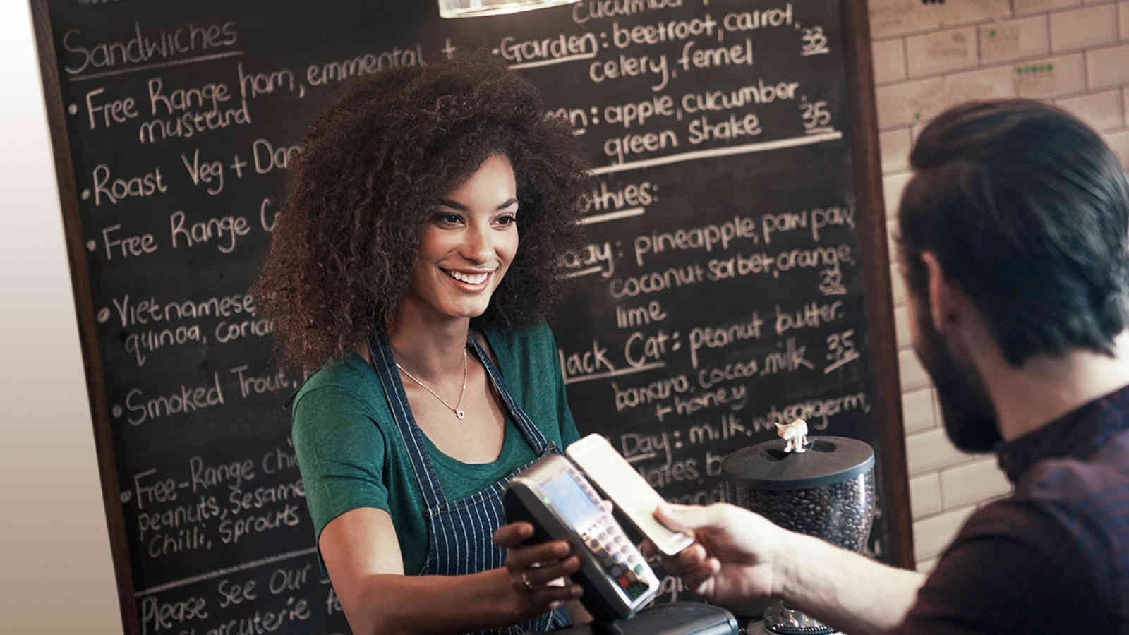 Woman holding a payment terminal for a man who is making a contactless mobile payment. Woman holding a payment terminal for a man who is making a contactless mobile payment.
