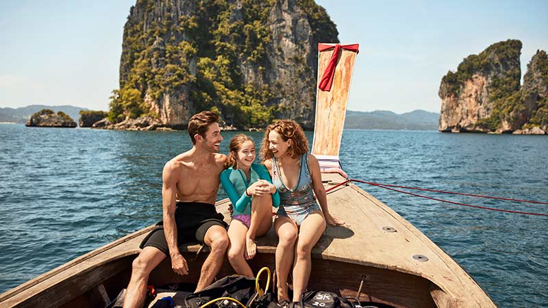 Travelling couple sitting at front of boat going through rock formations in the ocean